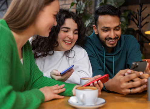 groupe de jeunes autour d'un café, regardant leurs smartphones et souriant